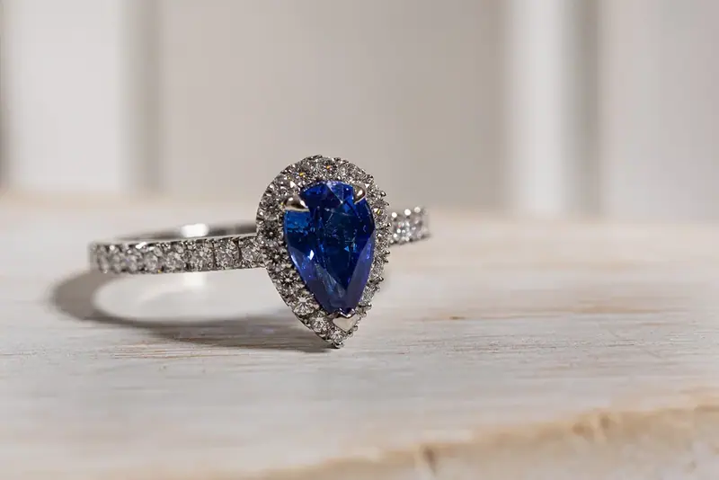 Pear-shaped blue sapphire ring with diamonds on a marble surface