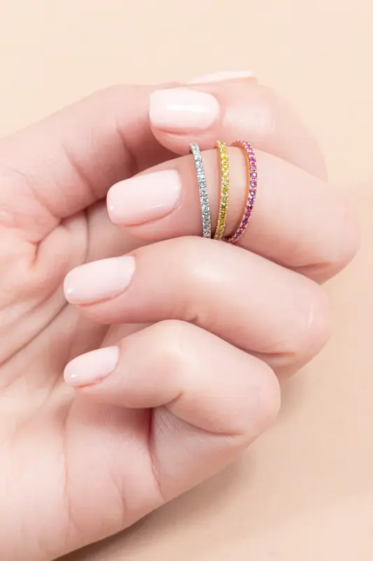 Hand holding three stacked gemstone rings, close-up