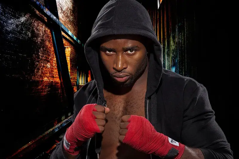 Boxer in a black hooded top wrapping his hands, dramatic lighting