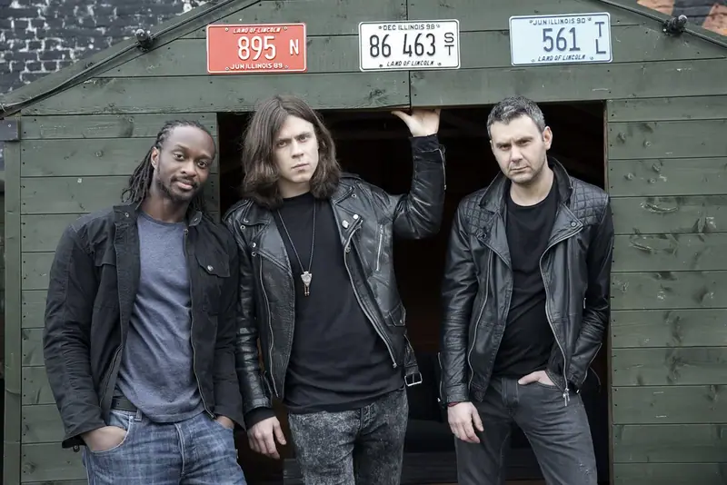 Four-piece band in dark clothing standing in front of a garage door