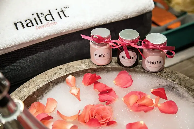 Nail polish bottles tied with ribbon beside a bowl of water and rose petals