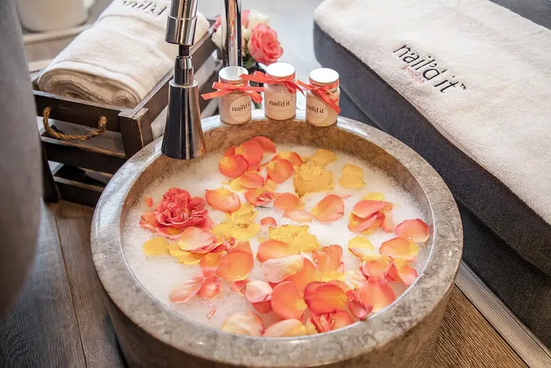 Nail polish bottles arranged beside a stone bowl of petals