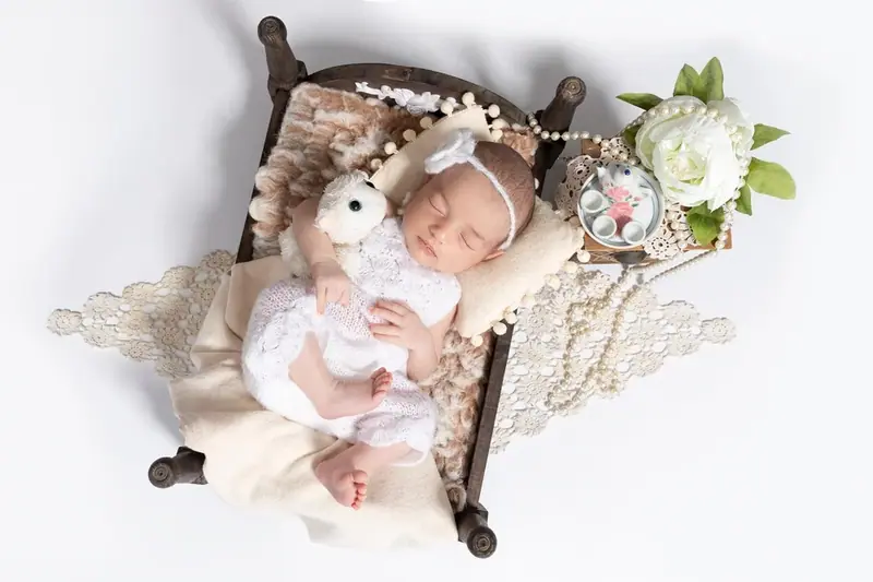 Newborn lying in a small wooden bed with white flowers and a soft toy