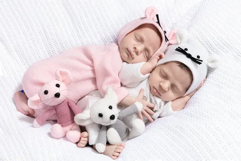 Newborn in a pink outfit with a knitted hat, lying beside two soft toys
