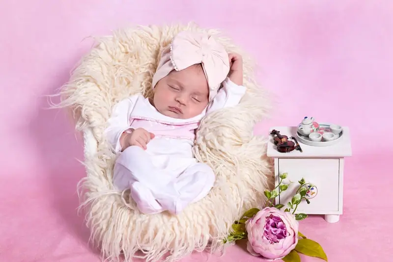 Newborn lying in a little white cot with a knitted toy under a lace canopy