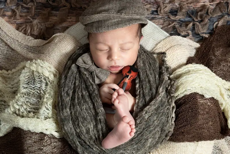 Newborn in a grey hat wrapped in a knitted blanket on a wooden backdrop