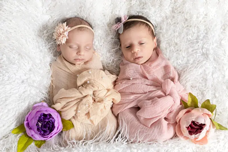 Newborn wearing a floral headband, wrapped in a pink blanket beside purple flowers