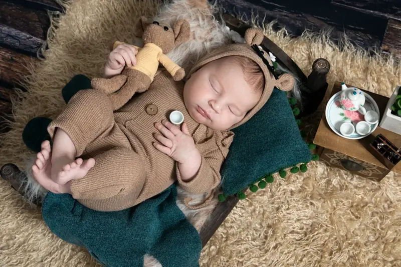 Newborn in a brown outfit lying on a green blanket with a wooden toy