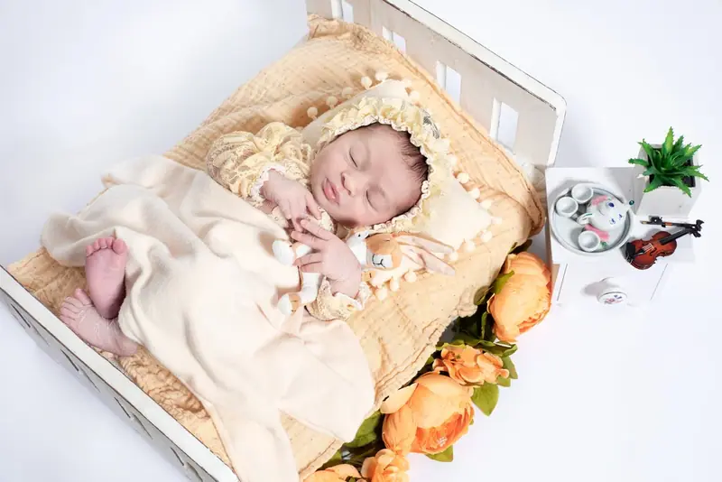 Newborn dressed in cream lying in a small wooden bed with a toy and flowers
