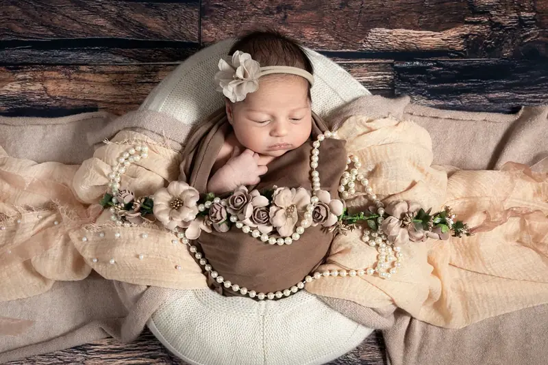 Newborn with a flower crown wrapped in brown, lying on cream fur