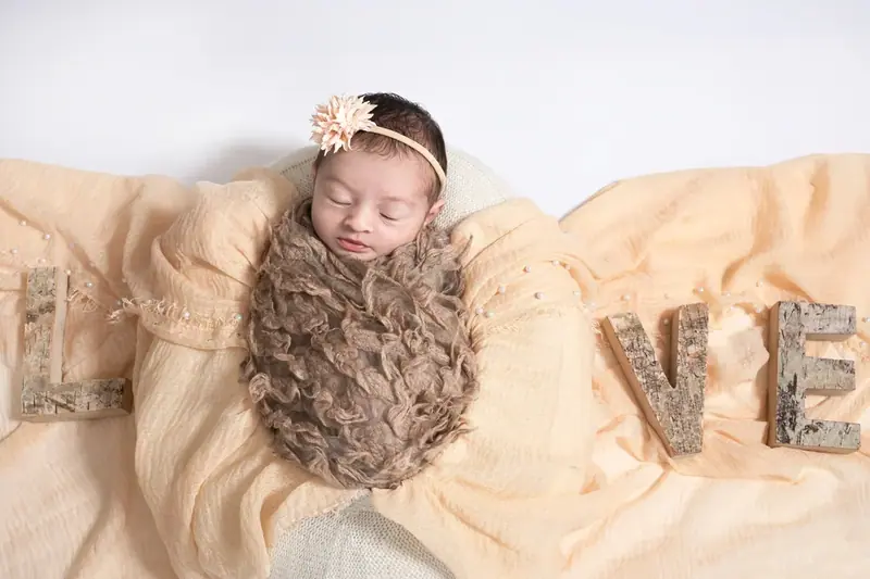 Newborn wrapped in brown fabric next to wooden letters spelling LOVE