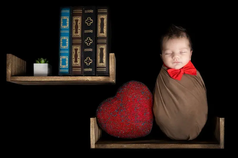 Newborn in a brown bear hat sitting on a wooden swing with a teddy bear