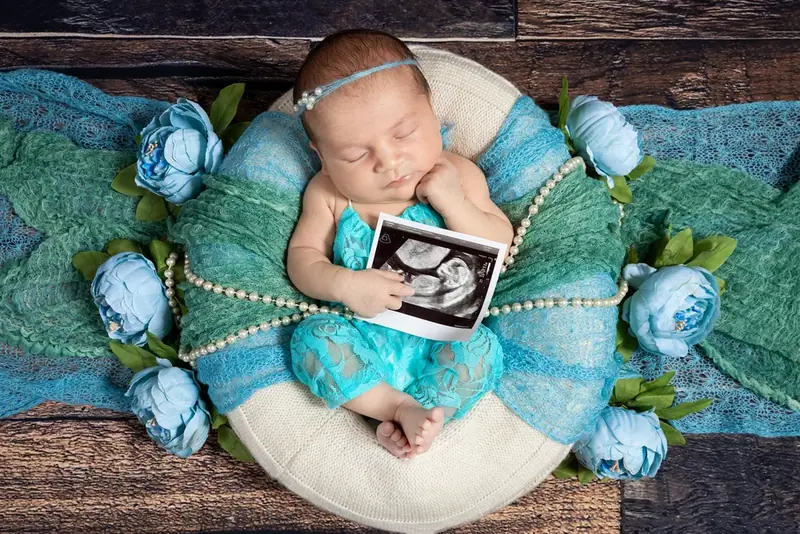 Newborn wrapped on white fur with blue flowers, holding a small picture