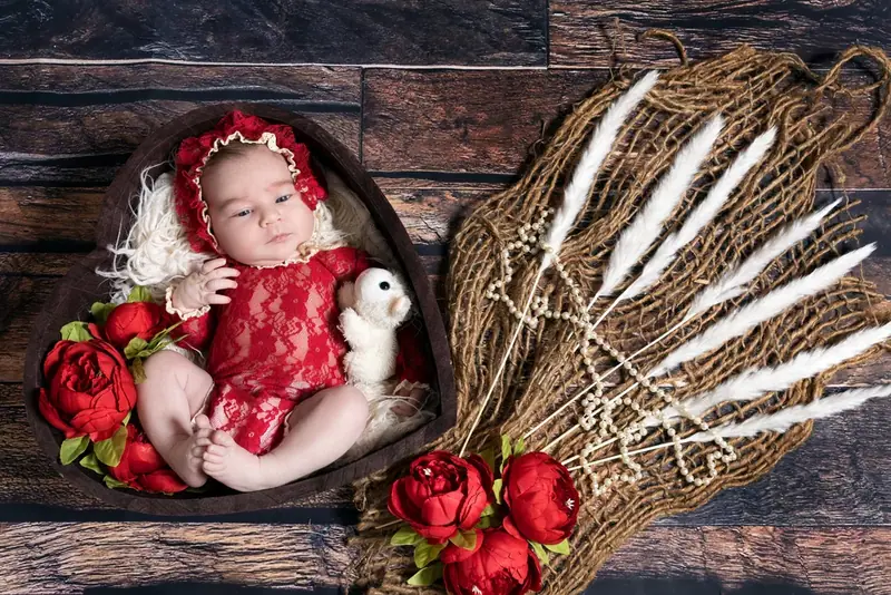 Newborn in a red outfit lying in a heart-shaped bowl with red roses and a toy rabbit