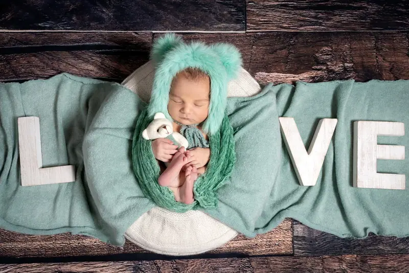 Newborn in a teal hat and wrap on a blanket with wooden letters spelling LOVE
