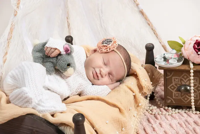 Newborn sleeping in a small wooden bed beside a toy and a mustard blanket