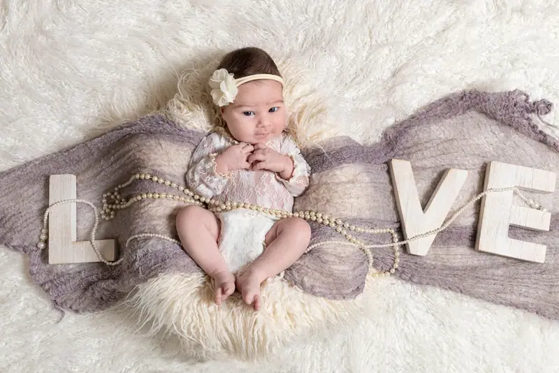 Newborn in a white outfit lying on a fur blanket with wooden letters spelling LOVE