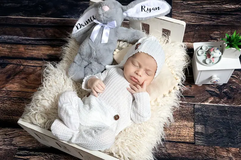 Newborn in white lying in a wooden crate with a knitted elephant toy