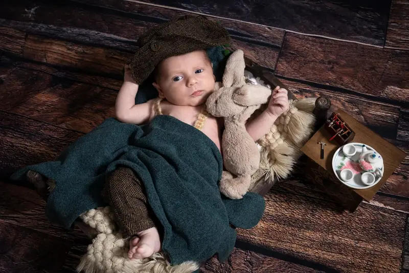 Newborn in a green outfit lying on a fur blanket with a toy rabbit