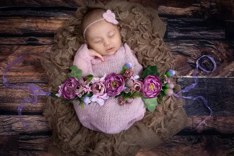 Newborn in a pink hat and wrap surrounded by purple and pink flowers