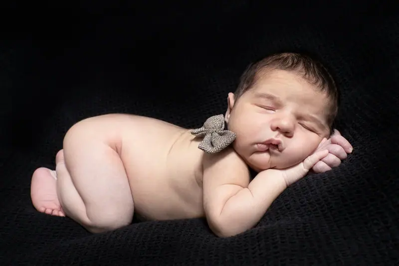 Newborn asleep on their tummy against a dark background