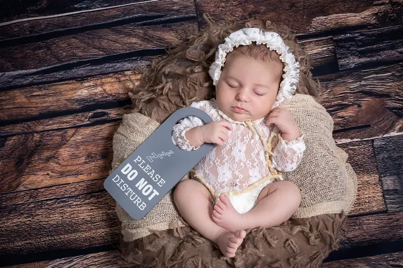 Newborn in a cream bonnet lying on a wooden floor holding a small chalkboard sign