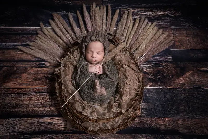 Newborn in a brown wrap curled up in a round nest of dried grasses