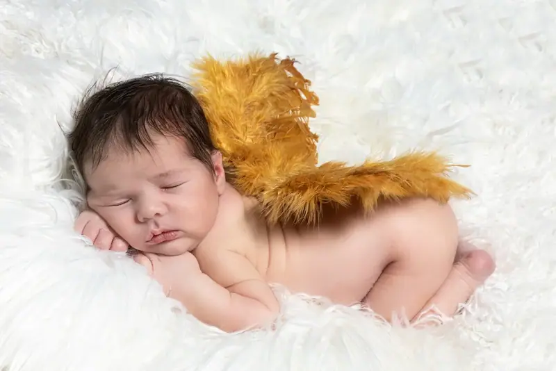 Newborn asleep on a white blanket wearing small golden angel wings