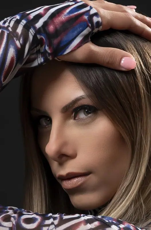 Close-up portrait of a woman resting a hand on her head, wearing a patterned top