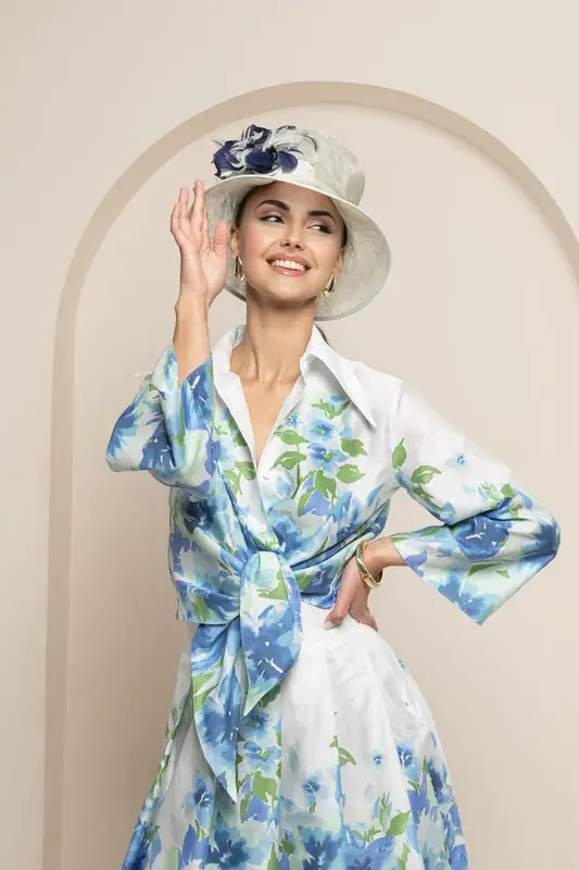 Woman in a blue floral dress and hat posing in front of a cream arch backdrop