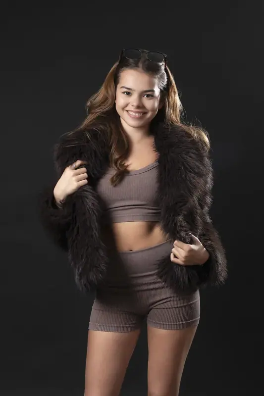 Woman in a dark fur jacket standing against a black studio backdrop