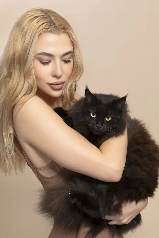 Woman with long blonde hair holding a black cat against a cream backdrop