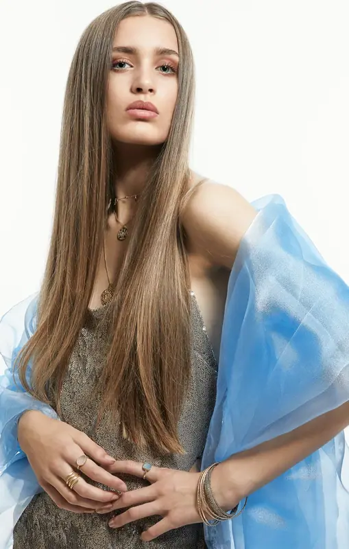 Woman with long hair holding a blue scarf in front of a cream arch backdrop