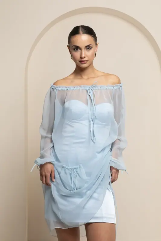 Woman in a light blue off-the-shoulder dress standing in front of a cream arch