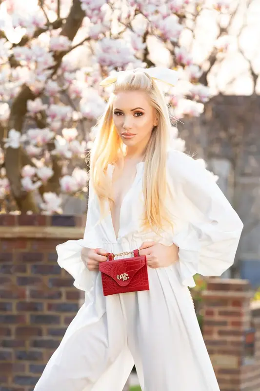 Woman in a white shirt holding a red bag beneath blossom trees