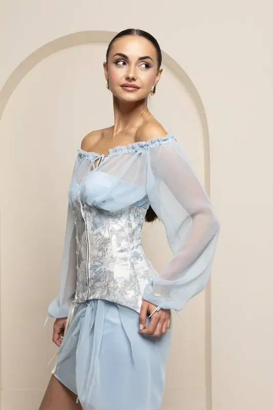 Woman in a light blue top and skirt standing in front of a cream arch