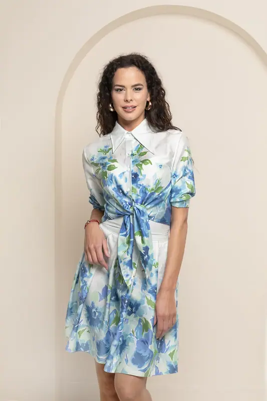 Woman in a blue floral dress standing in front of a cream arch backdrop