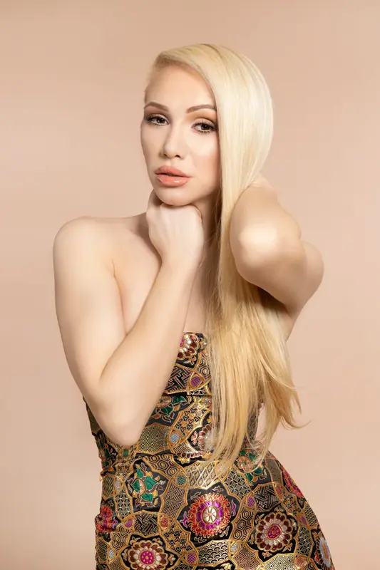 Blonde woman in a patterned dress posing in front of a cream backdrop