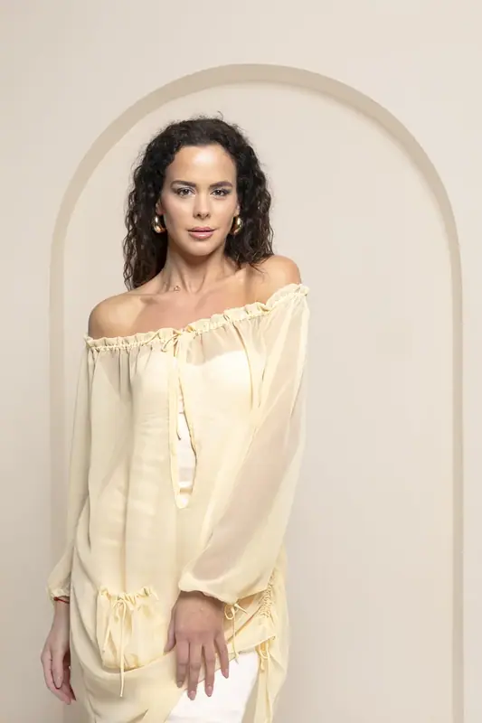 Woman in a pale yellow off-the-shoulder top standing in front of a cream arch