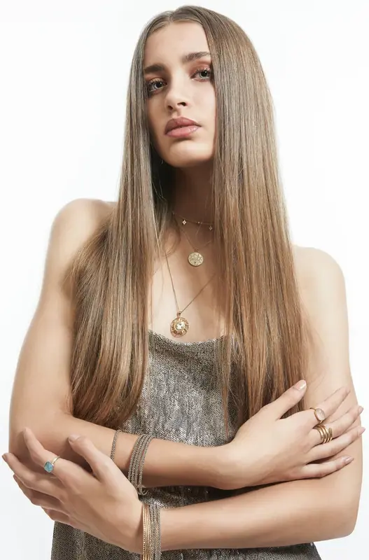 Woman with long straight hair in a grey top, arms folded, white background
