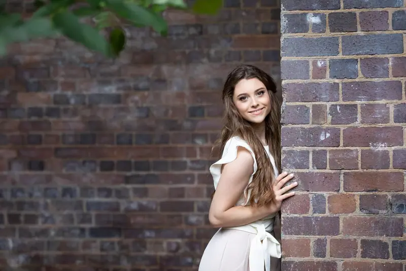 Woman in a white top standing beside a brick wall outdoors