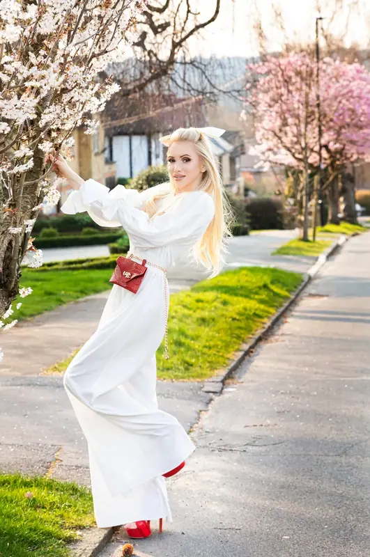Woman in white posing on a suburban street beneath blossom trees
