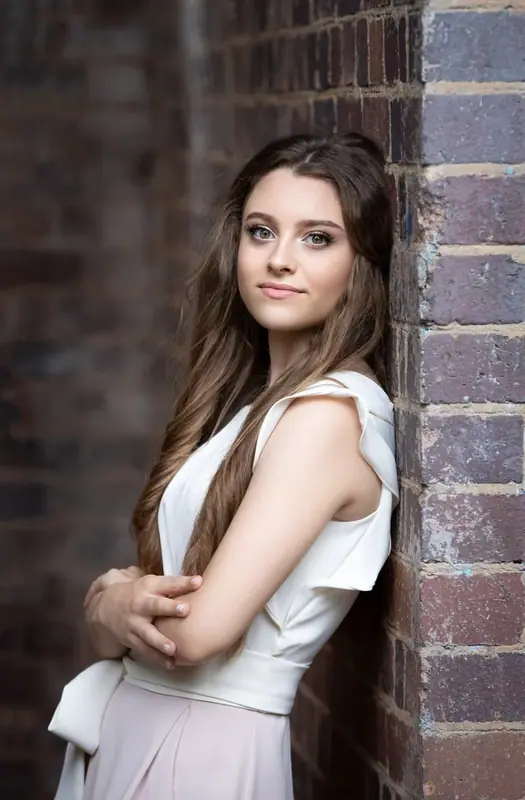 Woman in a white top standing against a brick wall with arms folded