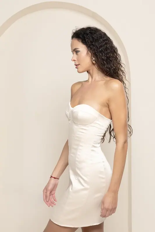 Woman in a white mini dress posing in front of a cream arch backdrop