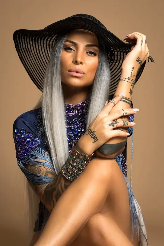 Woman in a wide-brimmed black hat and patterned top against a beige backdrop
