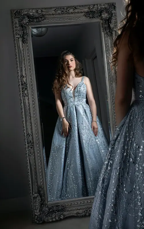 Woman in a pale blue gown reflected in a large ornate mirror