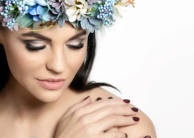 Close-up of a woman wearing a blue and purple flower crown with eyes closed