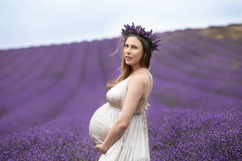 Expectant mother in a cream gown and flower crown standing in a lavender field