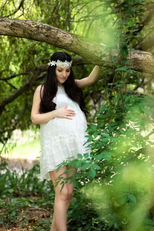 Expectant mother in white and a flower crown standing under a tree