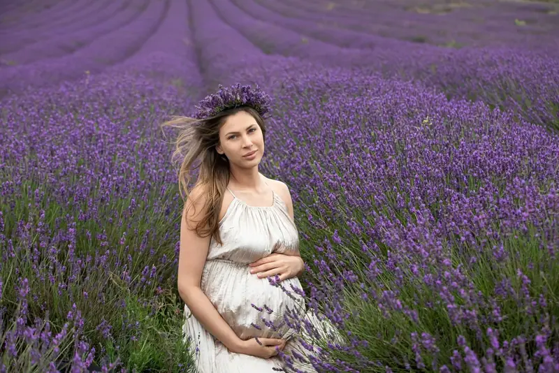 Expectant mother in a cream gown sitting in a lavender field